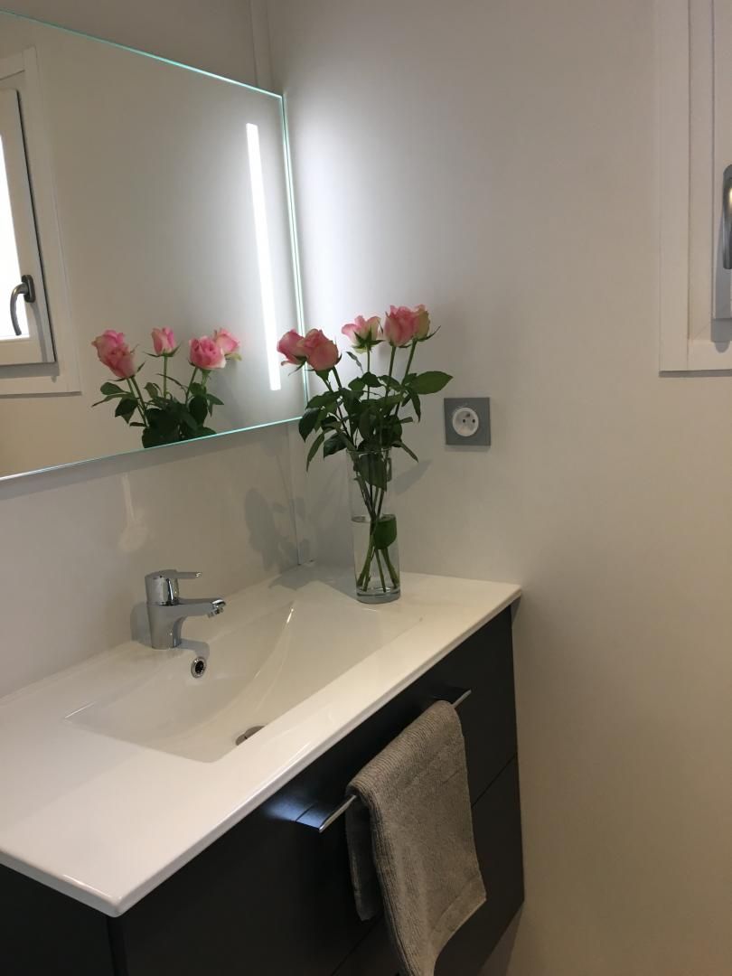A bathroom with a white sink, a mirror, and a vase with pink flowers.