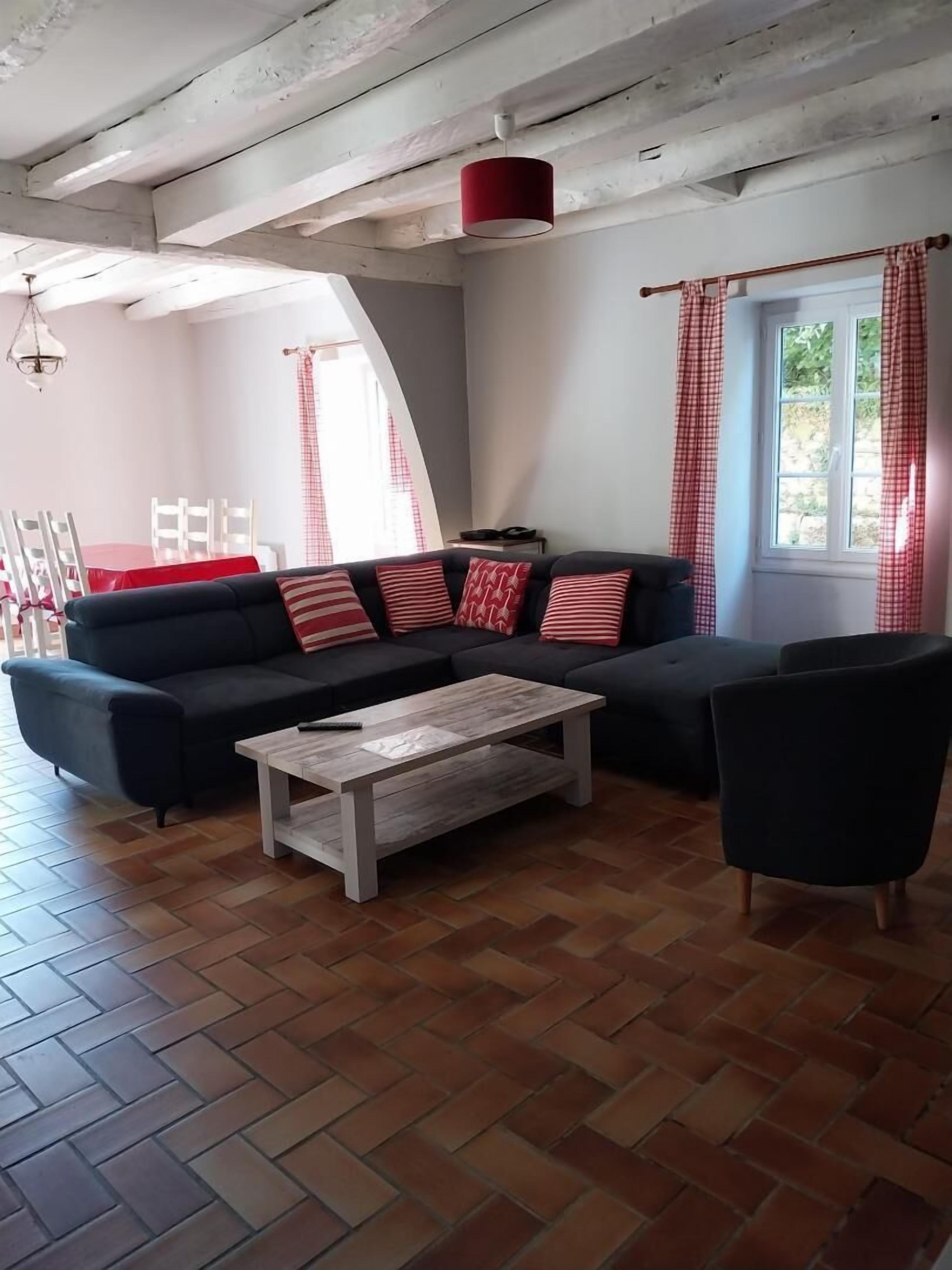 Una sala de estar con un sofá modular, una mesa de centro y un comedor con una mesa roja y sillas blancas.