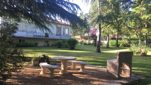 A garden with a stone table and benches, a stone wall, and a building with a balcony in the background. - Gîte du Parc - Chaunay (CHAUNAY)