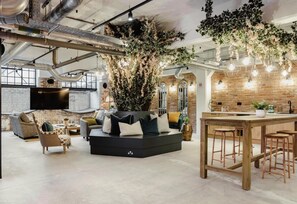 A modern living space with a large sofa, a dining area with stools, and a kitchen with a brick wall.