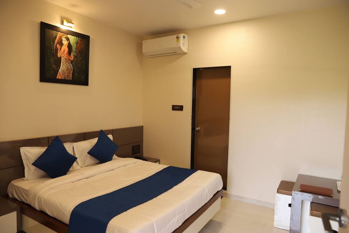 Hotelkamer met een bed, nachtkastje, bureau, airconditioning, deur en een schilderij aan de muur.