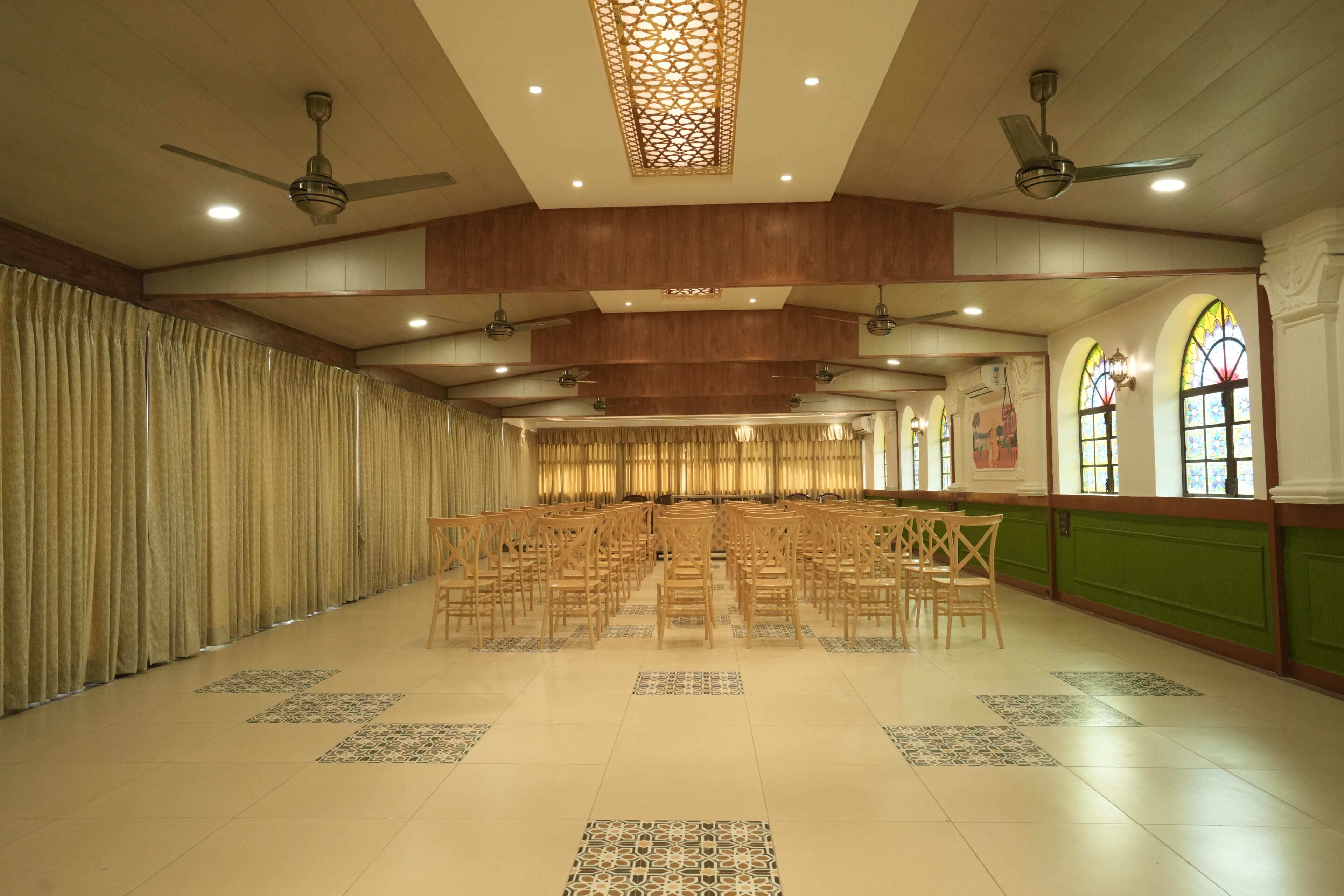 A spacious hall with rows of chairs, wooden paneling, and decorative ceiling elements.