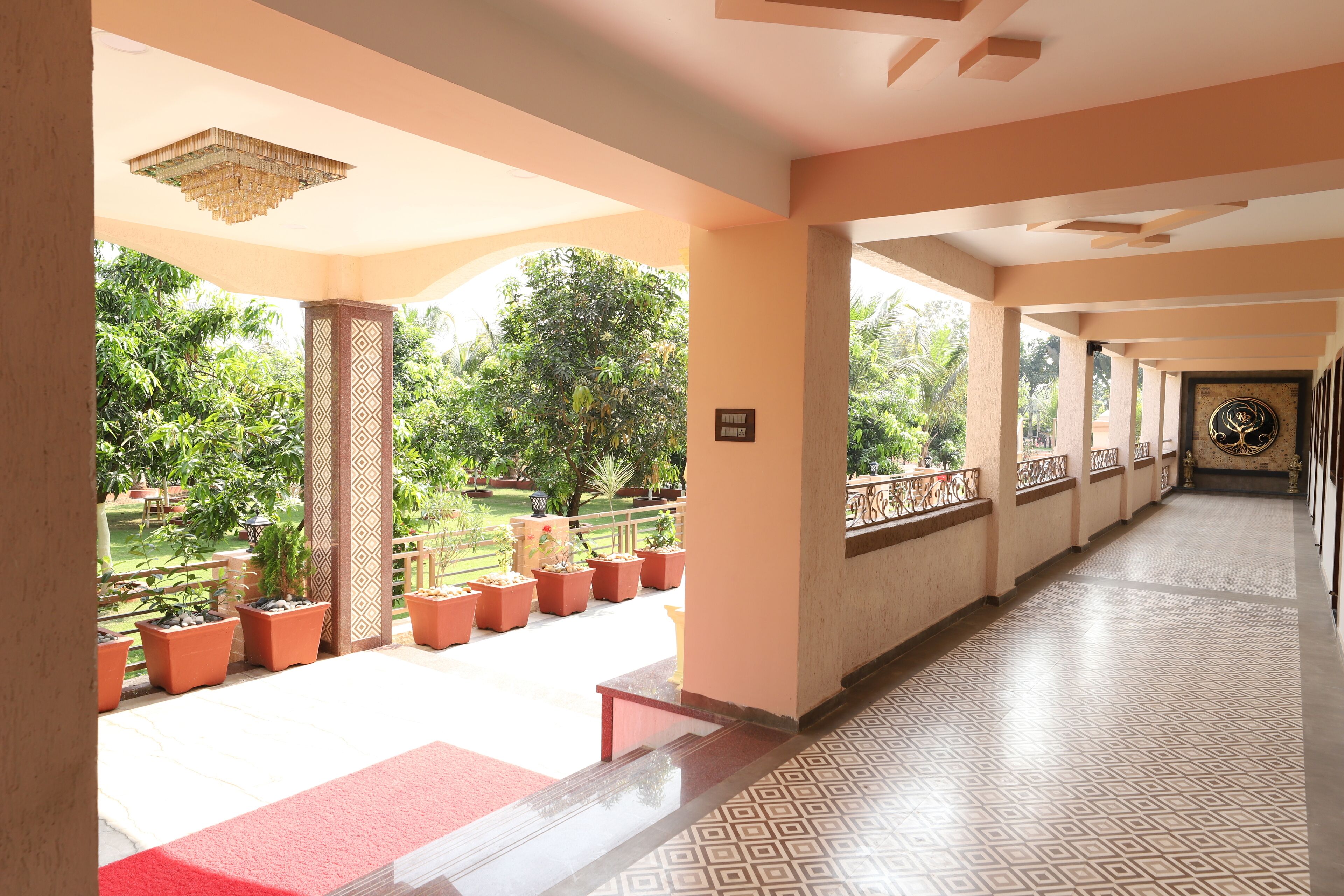 A corridor with a patterned floor, columns with geometric designs, and potted plants along the walkway.
