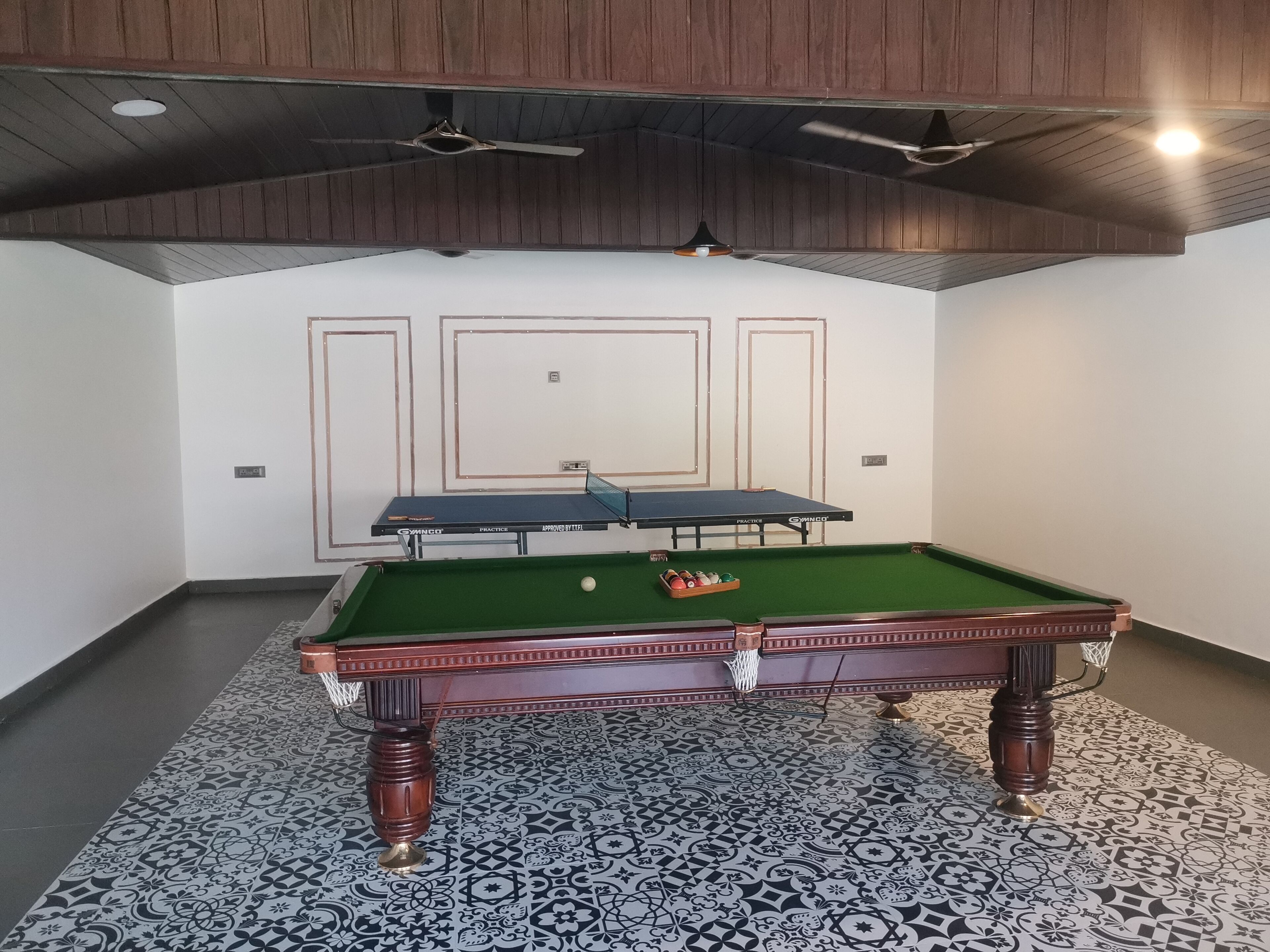 A pool table with a green felt surface, a white wall with a door, and a ceiling fan.
