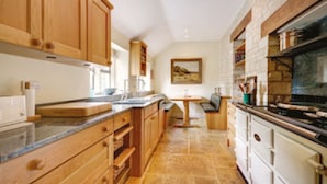 A kitchen with wooden cabinets, a granite countertop, and a stove. - Charming cottage in the heart of the Cotswolds (Cirencester)