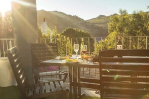 An outdoor dining area with a table set for two, surrounded by wooden chairs, overlooking a scenic landscape with hills and trees. - Family Suite w/ Pool, Hot Tub, fireplace & Valley Views (Cape Town)
