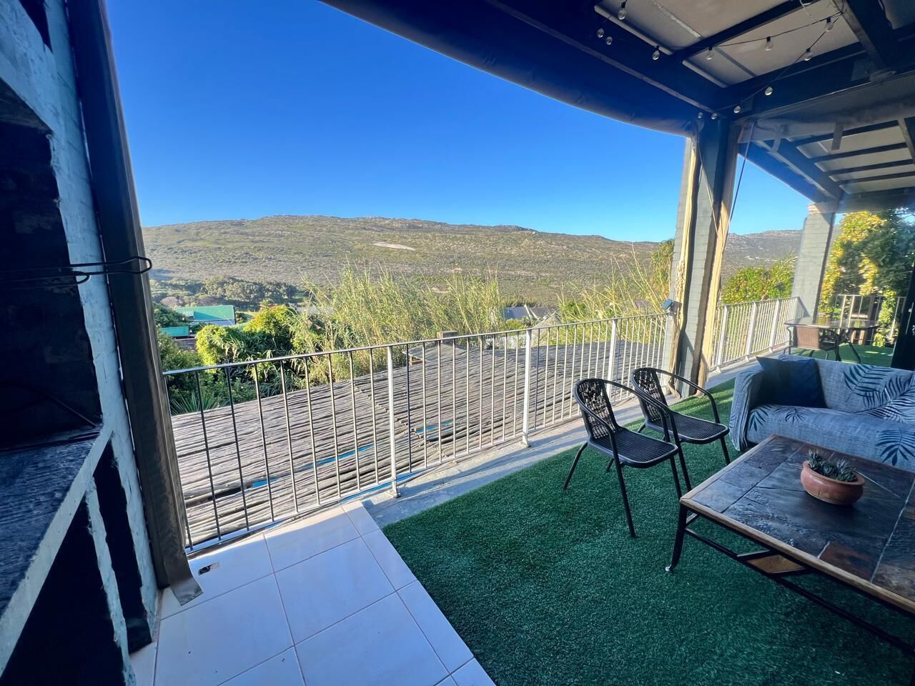 A balcony with a view of hills, a table with chairs, and a potted plant.