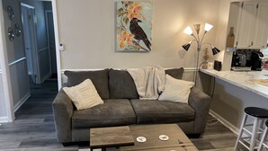 A living room with a grey sofa, a coffee table, and a painting of a bird on the wall. - Cozy house close to everything you need for a comfortable stay. (Columbus)