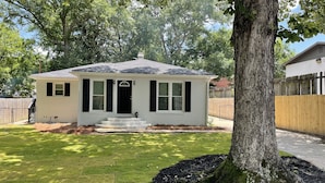 A single-story house with a front porch, a small front yard, and a wooden fence. - Cozy house close to everything you need for a comfortable stay. (Columbus)