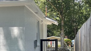 A residential area with a white brick house, two trash bins, and a wooden fence. - Cozy house close to everything you need for a comfortable stay. (Columbus)