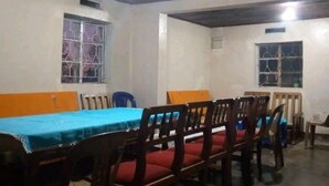Un comedor con una mesa larga y sillas, un mantel azul y ventanas con rejas.