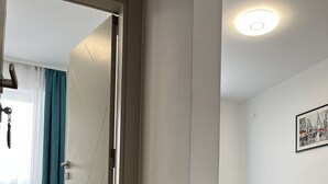 A hotel room with two beds, a wooden floor, a white wall, and a ceiling light. - Dona (Belgrade)