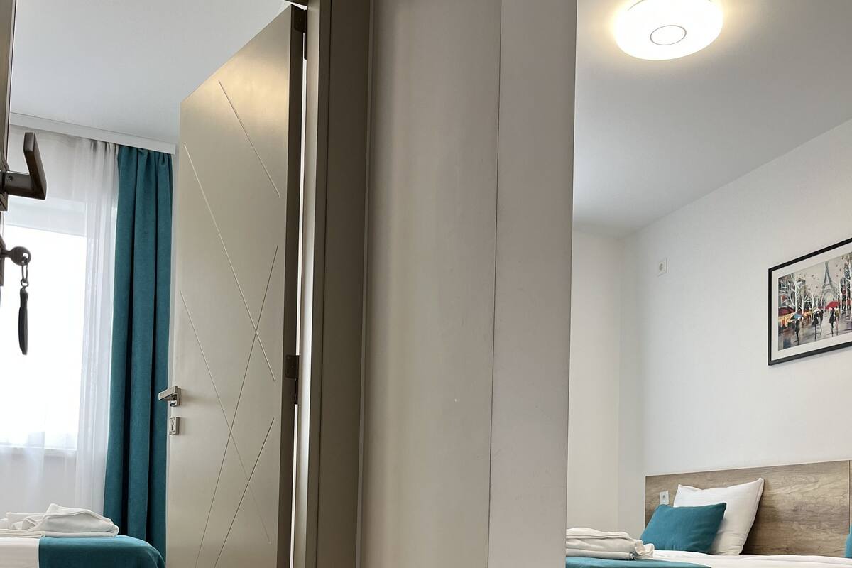 A hotel room with two beds, a wooden floor, a white wall, and a ceiling light.