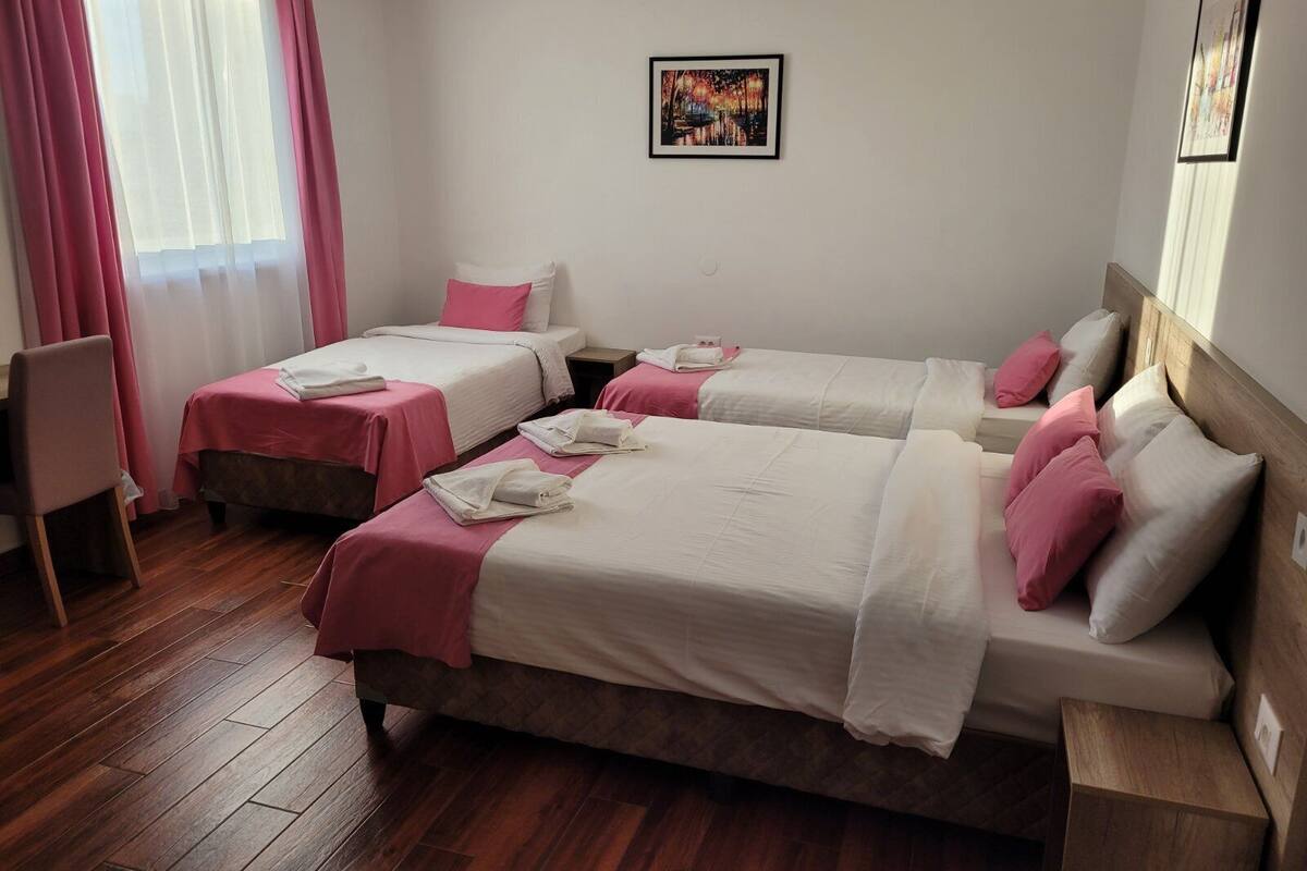 A hotel room with two beds, wooden flooring, and a painting on the wall.