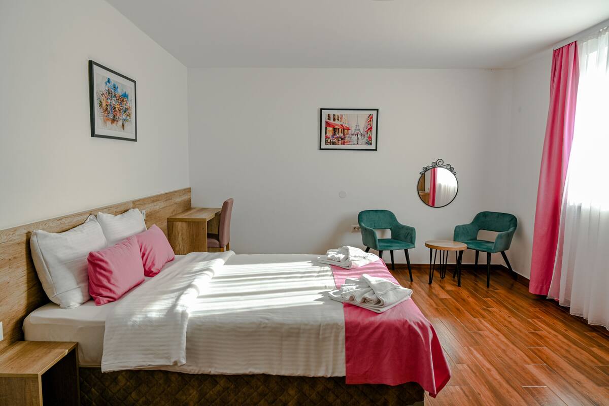 A hotel room with a bed, two chairs, a small table, and two framed pictures on the walls.