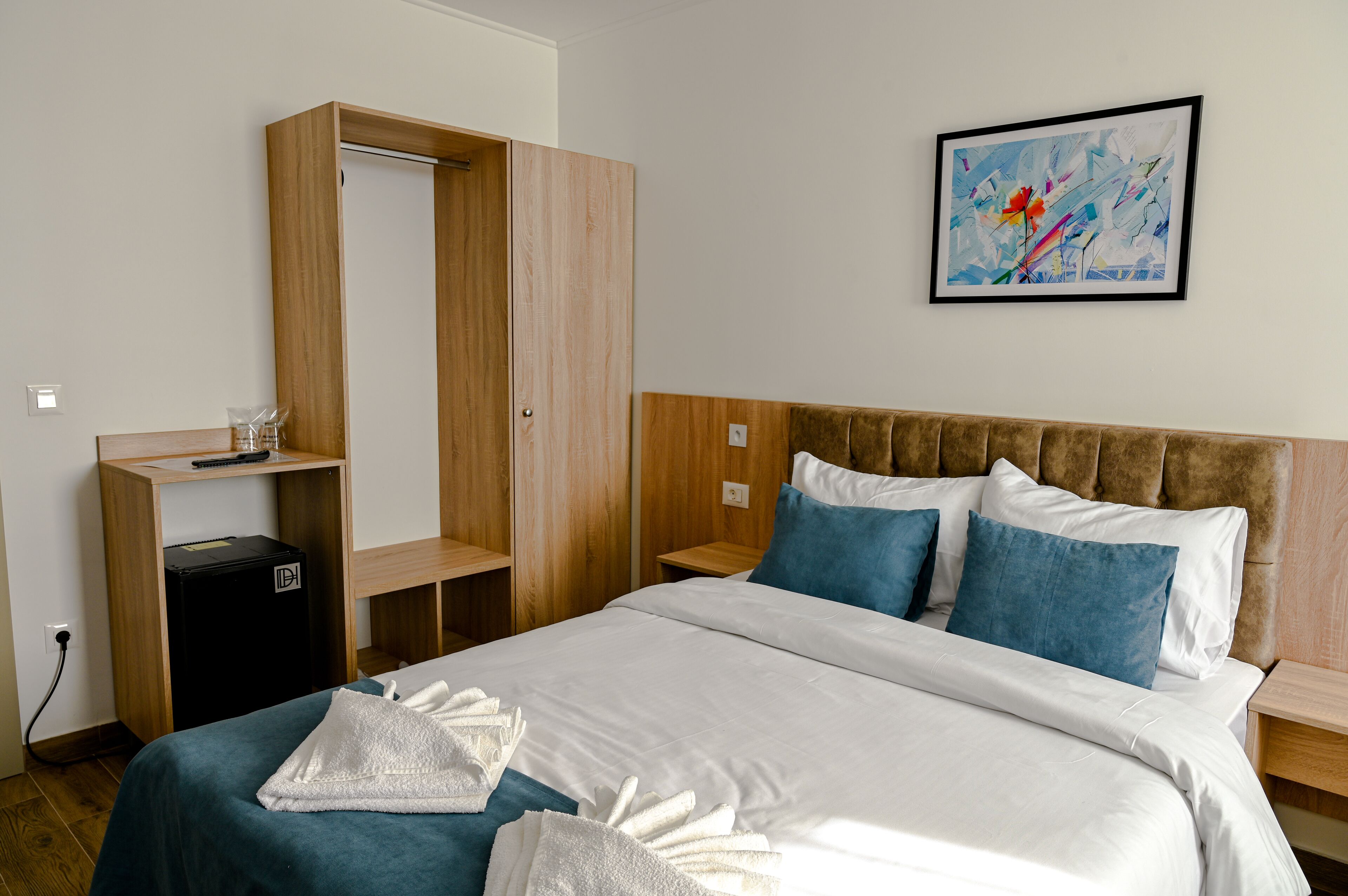 Quarto de hotel com cama, guarda-roupa, escrivaninha e um quadro na parede.