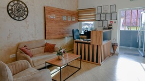 A hotel reception area with a wooden reception desk, a sofa, a coffee machine, and a wall clock. - Dona (Belgrade)