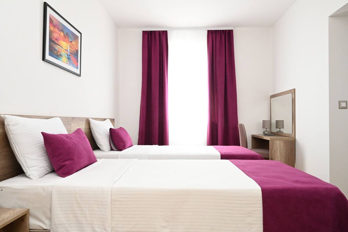 A hotel room with two beds, a desk, a chair, a mirror, and a painting on the wall.
