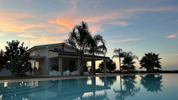 A modern house with a pool, surrounded by palm trees and a clear sky.