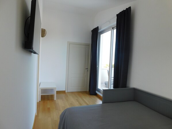 A room with a bed, a television mounted on the wall, a door, and a window with curtains.
