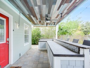 A covered patio with a built-in bench and table, a red door, and a view of the backyard.