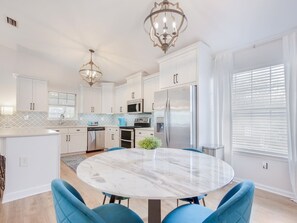 A modern kitchen with white cabinetry, a marble island, and blue chairs.