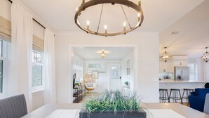 A modern living room with a central plant arrangement, a dining area, and a kitchen visible through an open doorway.
