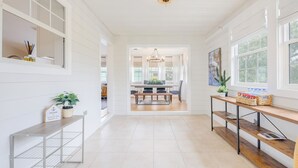 A spacious, well-lit room with a wooden floor, a dining area in the background, and a bench with a sign on the left.