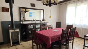 Un comedor con suelo de baldosas hexagonales, una mesa con mantel rojo, sillas de madera, una araña y una chimenea con chimadas.