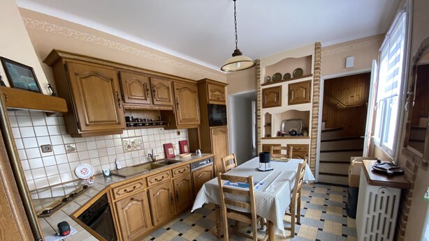 Una cocina con armarios de madera, salpicadero de azulejos, una mesa de comedor con sillas y un radiador.