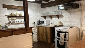 Cozinha com fogão, forno, micro-ondas e prateleiras de madeira com louças.