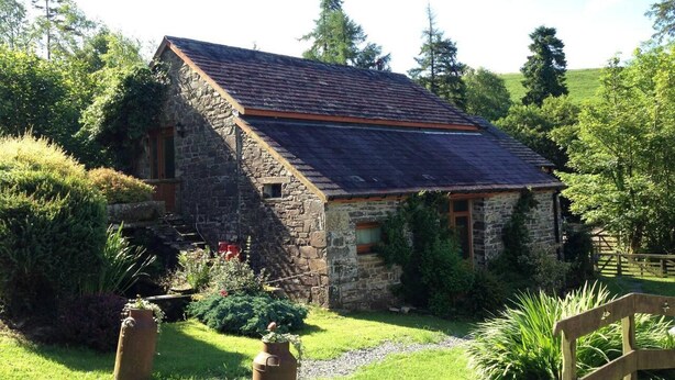 A stone house with a sloped roof, surrounded by lush greenery and a wooden fence. - Relaxing Holidays in the Old Water Mill at Cwmiar (Llanybydder)
