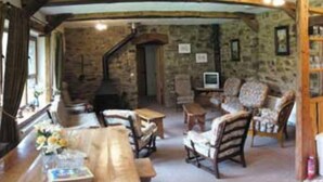 A rustic stone interior with a fireplace, wooden furniture, and a television. - Relaxing Holidays in the Old Water Mill at Cwmiar (Llanybydder)