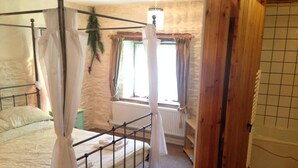A four-poster bed with white linens, a wooden floor, a stone wall, and a window with curtains. - Relaxing Holidays in the Old Water Mill at Cwmiar (Llanybydder)