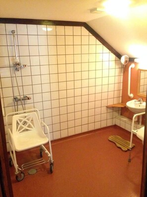 Een kleine betegelde badkamer met een douche, een wastafel en een rolstoel.