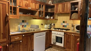 A kitchen with wooden cabinets, a dishwasher, a stove, and a microwave. - Relaxing Holidays in the Old Water Mill at Cwmiar (Llanybydder)