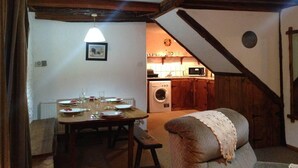 Un comedor acogedor con una mesa de madera dispuesta para cuatro personas, un sofá con una manta, y una cocina al fondo con lavadora y microondas.