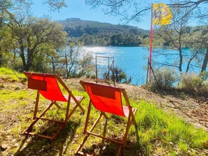 Zwei rote Klappstühle auf einem grasbewachsen Hügel mit Blick auf einen See und eine Flagge.