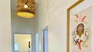 A hallway with a wooden floor, a hanging woven light fixture, and a framed artwork on the wall.