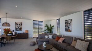 A modern living room with a sectional sofa, a dining area with a table and chairs, and artwork on the walls.