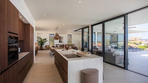 A modern kitchen with a central island, a dining area with a large table, and a view of the outdoor patio.