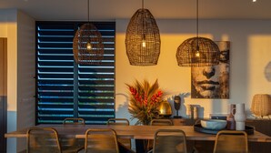 A modern dining area with a wooden table, six wicker chairs, and two hanging pendant lights.