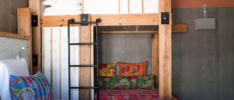 Uma cama de solteiro com escada, cabeceira de madeira e colcha colorida.