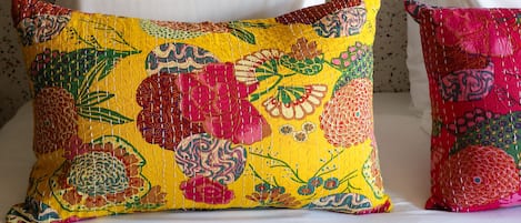 Ein Bett mit weißen Kissen und zwei farbenfrohen Kissen mit Blumenmuster.