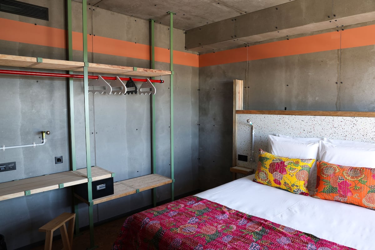 A bedroom with a bed, a wooden bench, a hanging rack, and a small table.