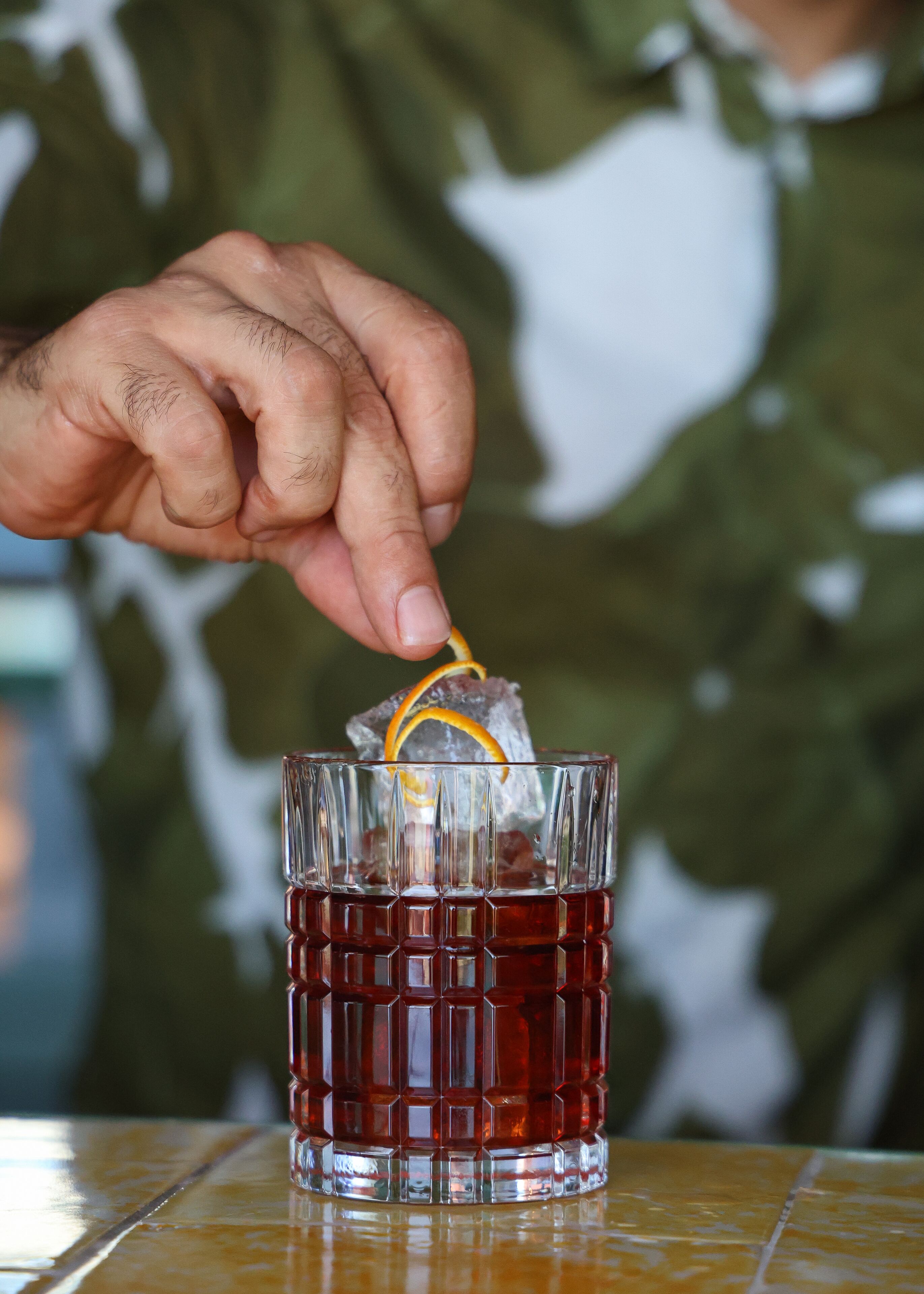 Une main presse une tranche d’orange dans un verre contenant une boisson rouge.