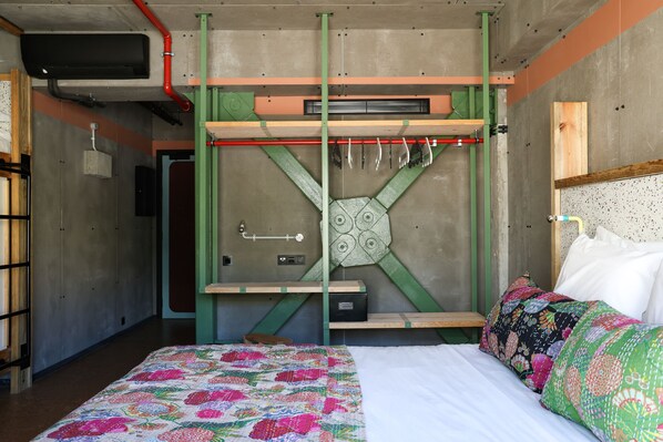 A bedroom with a bed, a quilt, a headboard, and a wooden shelf with a mirror.
