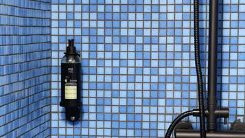 Casa de banho com azulejos de mosaico azuis, uma garrafa preta de máquina de café Keurig e um chuveiro.