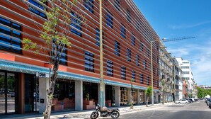 A modern building with a red facade, large windows, and a motorcycle parked on the sidewalk. - Jam Hotel Lisbon (Lisbon)