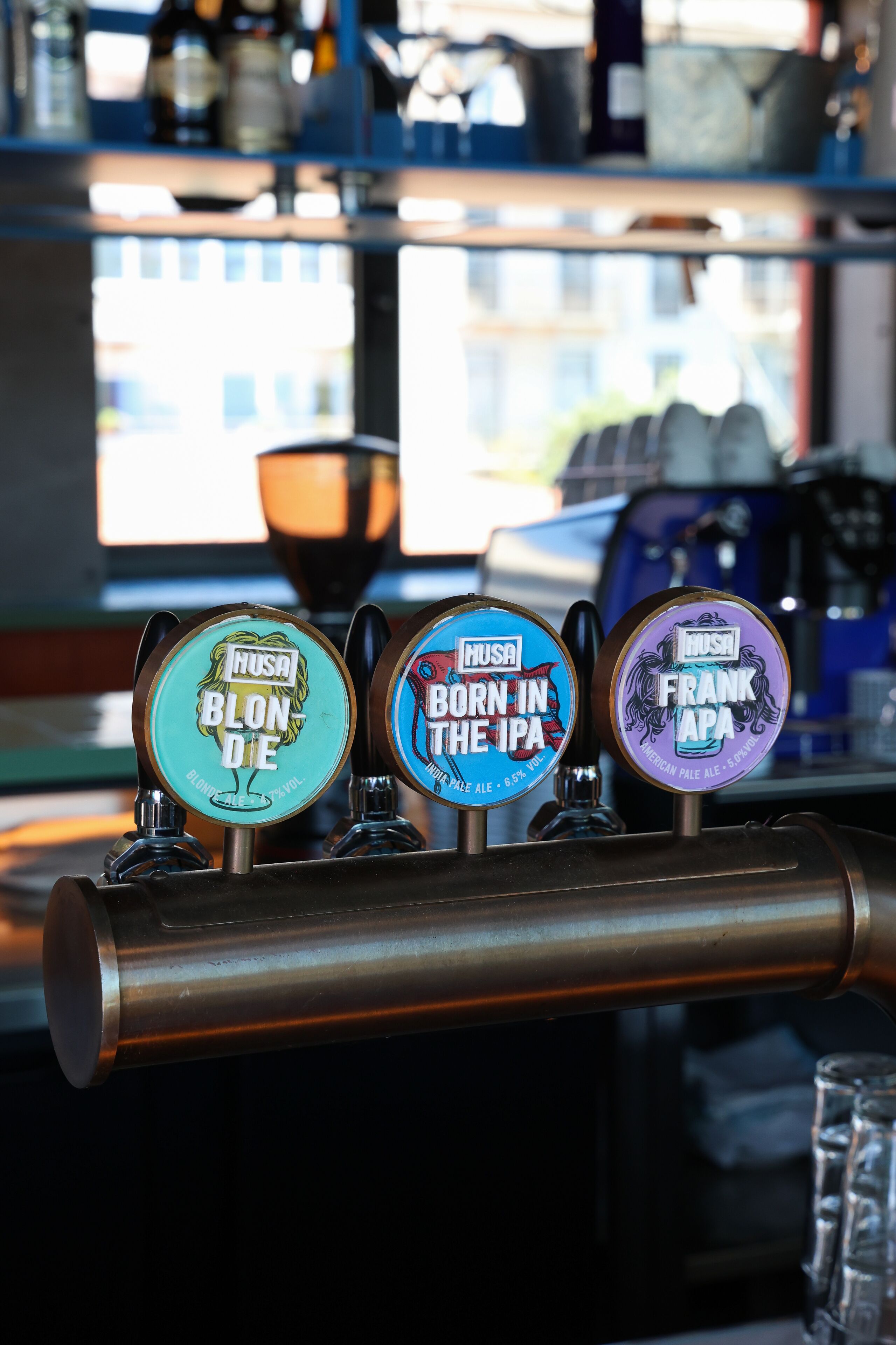 A bar with three taps labeled 'NUSA Blondie,' 'NUSA Born in the IPA,' and 'NUSA Frank APA.'